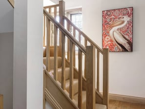 A wooden staircase with a woven carpet, a wall-mounted artwork of a bird, and a window with blinds. - The Lady Rothschild Stables (Peterborough)