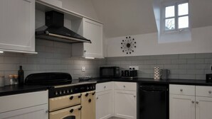 Uma cozinha com armários brancos, fogão preto, micro-ondas e lava-louças.