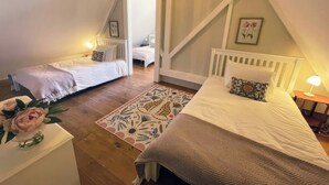 Quarto com duas camas, piso de madeira, tapete estampado e uma pequena mesa com abajur.
