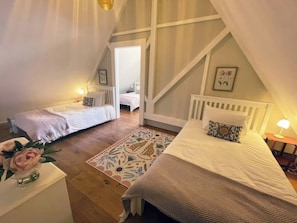 A bedroom with two beds, a wooden floor, a patterned rug, and a small table with a lamp. - The Lady Rothschild Stables (Peterborough)