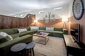 A living room with a sectional sofa, a coffee table, two side tables, a TV, and decorative wall art. - The Lady Rothschild Stables (Peterborough)