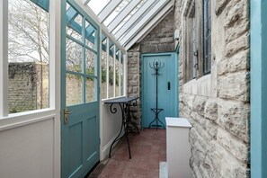 A conservatory with a teal door, a coat rack, and a small table. - Greenwood Manor (Peterborough)