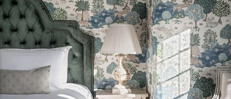 A bedroom with a tufted headboard, a bedside table with a lamp, and a window with patterned curtains.