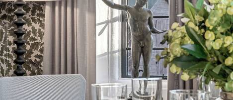 Un coin repas avec une table dressée pour deux personnes, une statue et une fenêtre avec des rideaux.