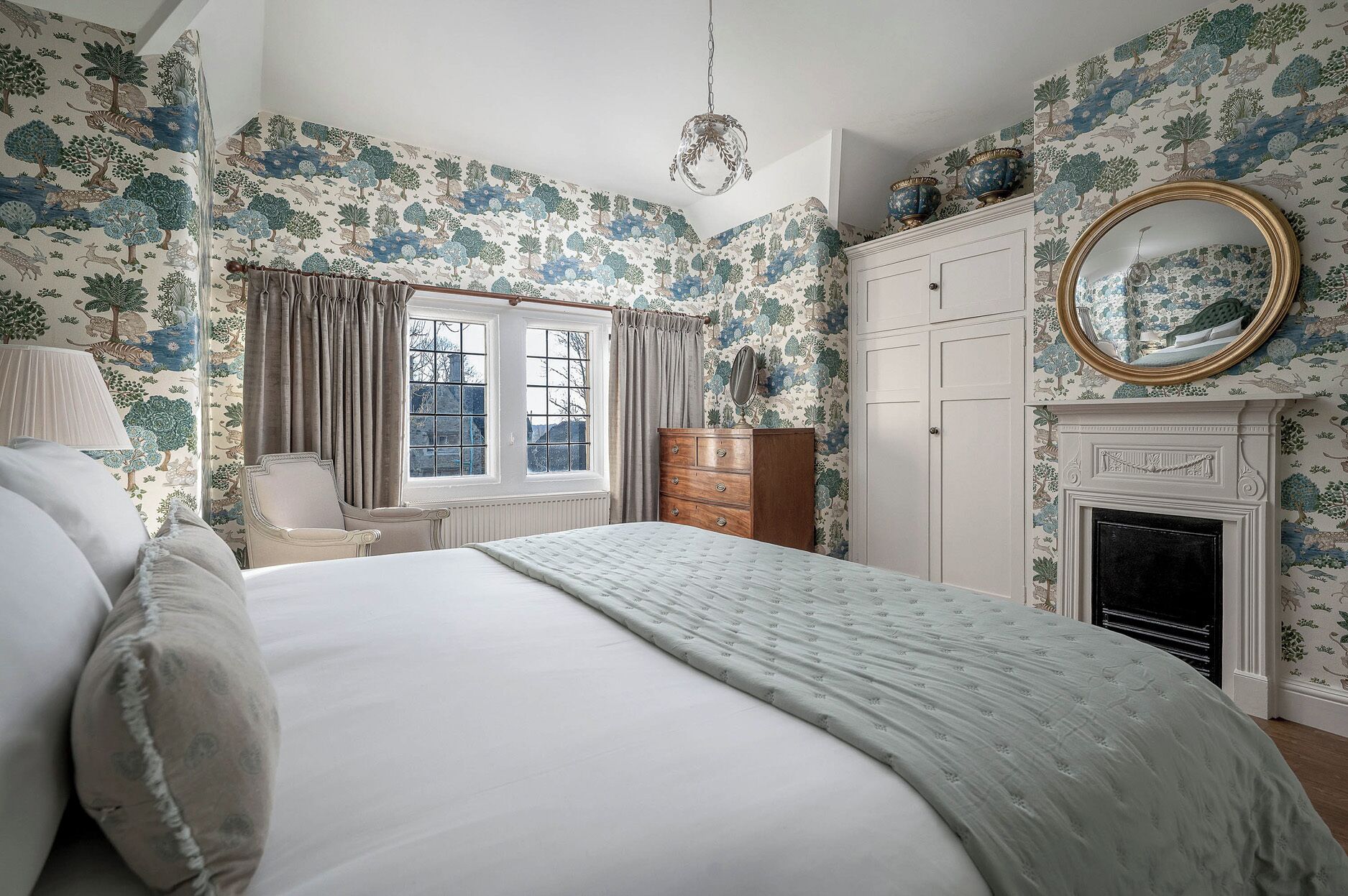 A bedroom with a bed, dresser, mirror, and fireplace.