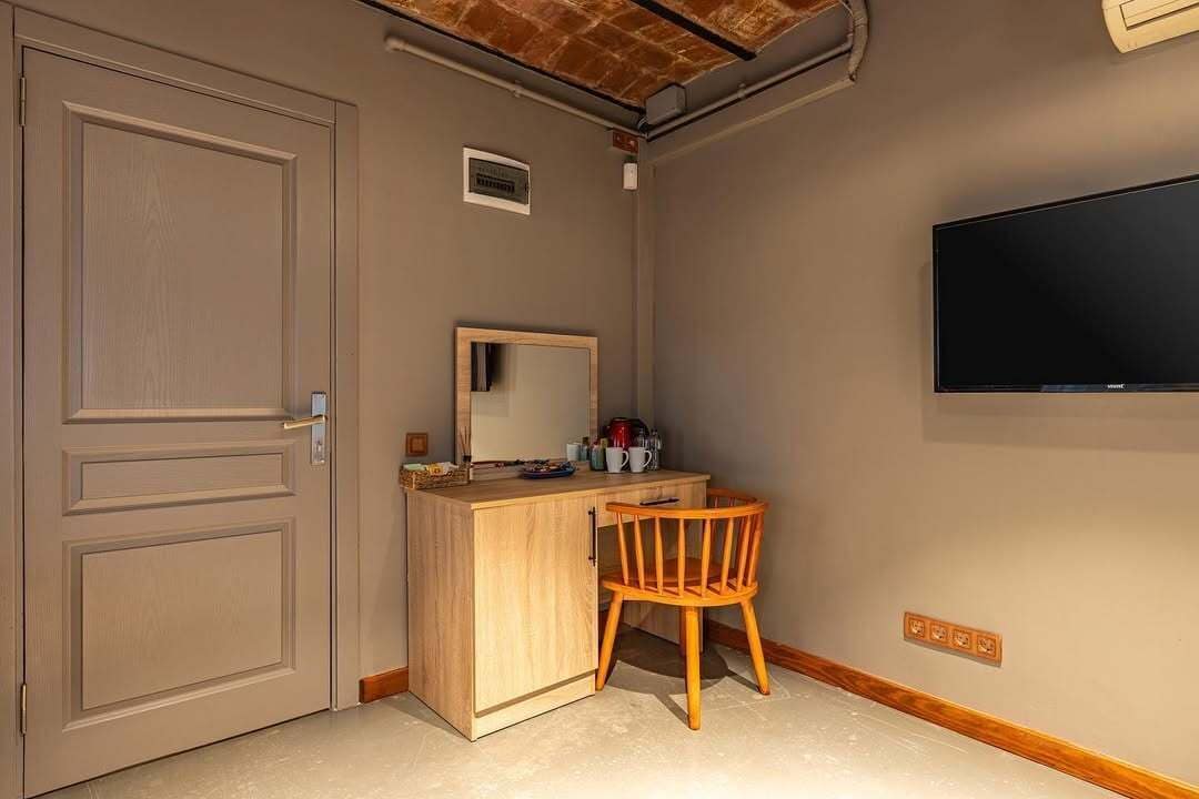 A room with a wooden desk, a chair, a television, and a door.
