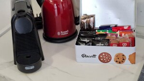 Una cocina con una cafetera roja Russell Hobbs, una máquina de espresso Delonghi y una caja de biscotti.