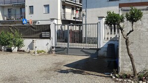 Una entrada protegida por una reja a un edificio, con una señal de paso para peatones, un pequeño árbol y un camino de grava.