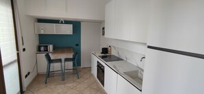 Una cucina compatta con forno a microonde, lavello e un piccolo angolo ristoro con sedie.