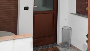 Una entrada limpia y moderna con una puerta de madera, un cubo de basura pequeño y un felpudo.