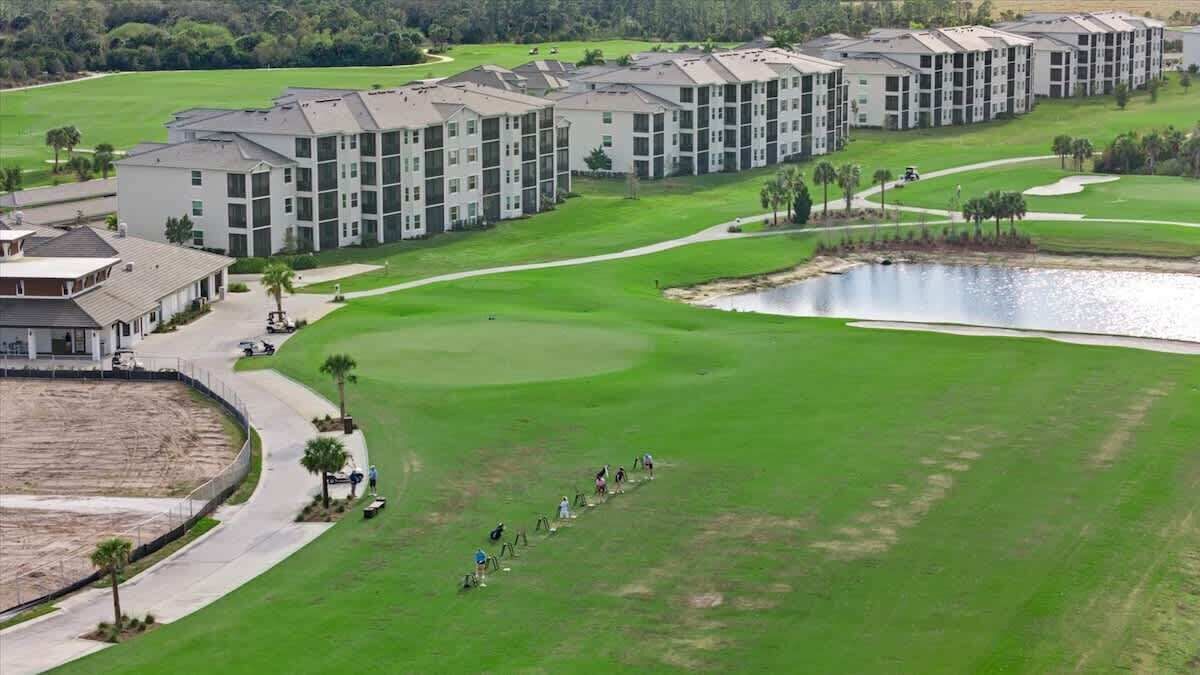 A golf course with a water hazard, a clubhouse, and a row of apartment buildings.