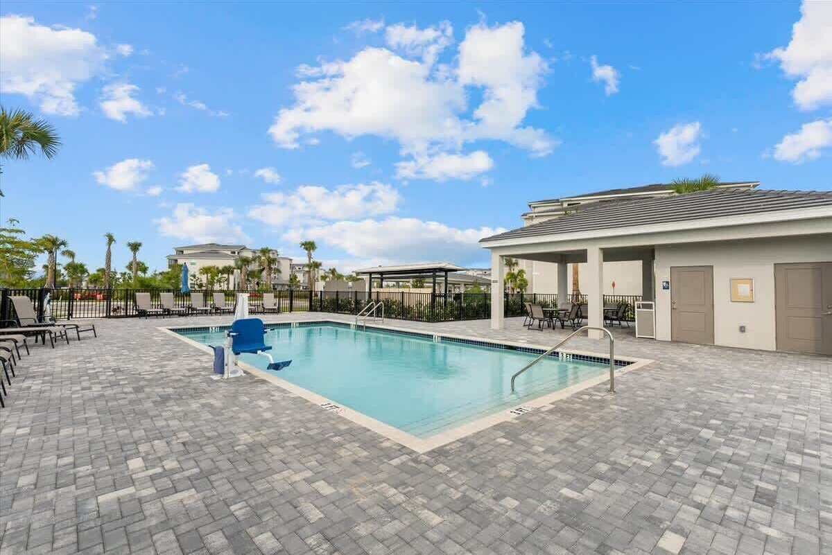 A swimming pool with lounge chairs and a covered area, surrounded by a paved deck and palm trees.