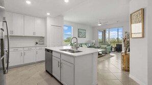 Een moderne keuken met witte kastjes, een centraal eiland met een spoelbak en een zithoek met een groene bank.