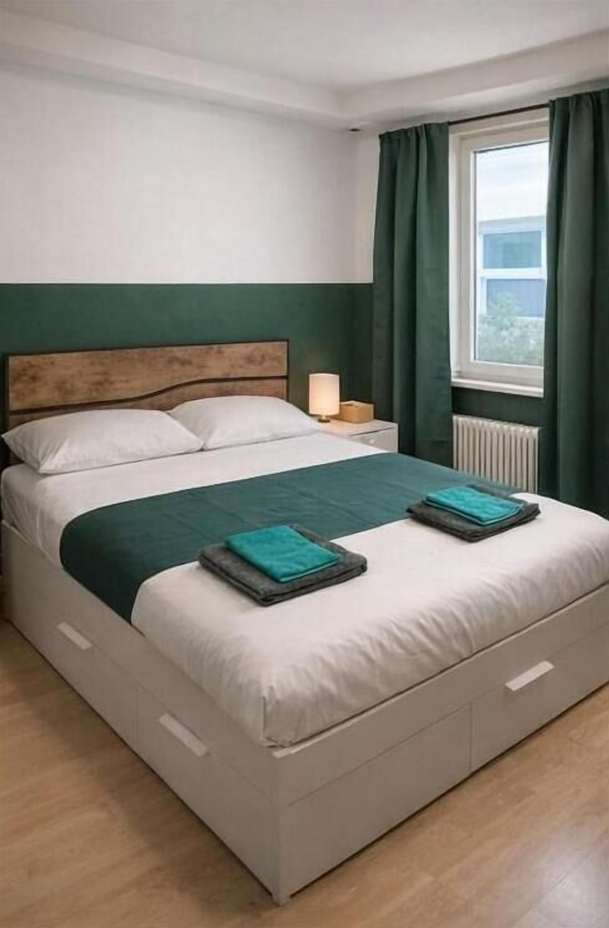 Un lit avec une tête de lit en bois, une table de chevet avec une lampe et une fenêtre avec des rideaux.