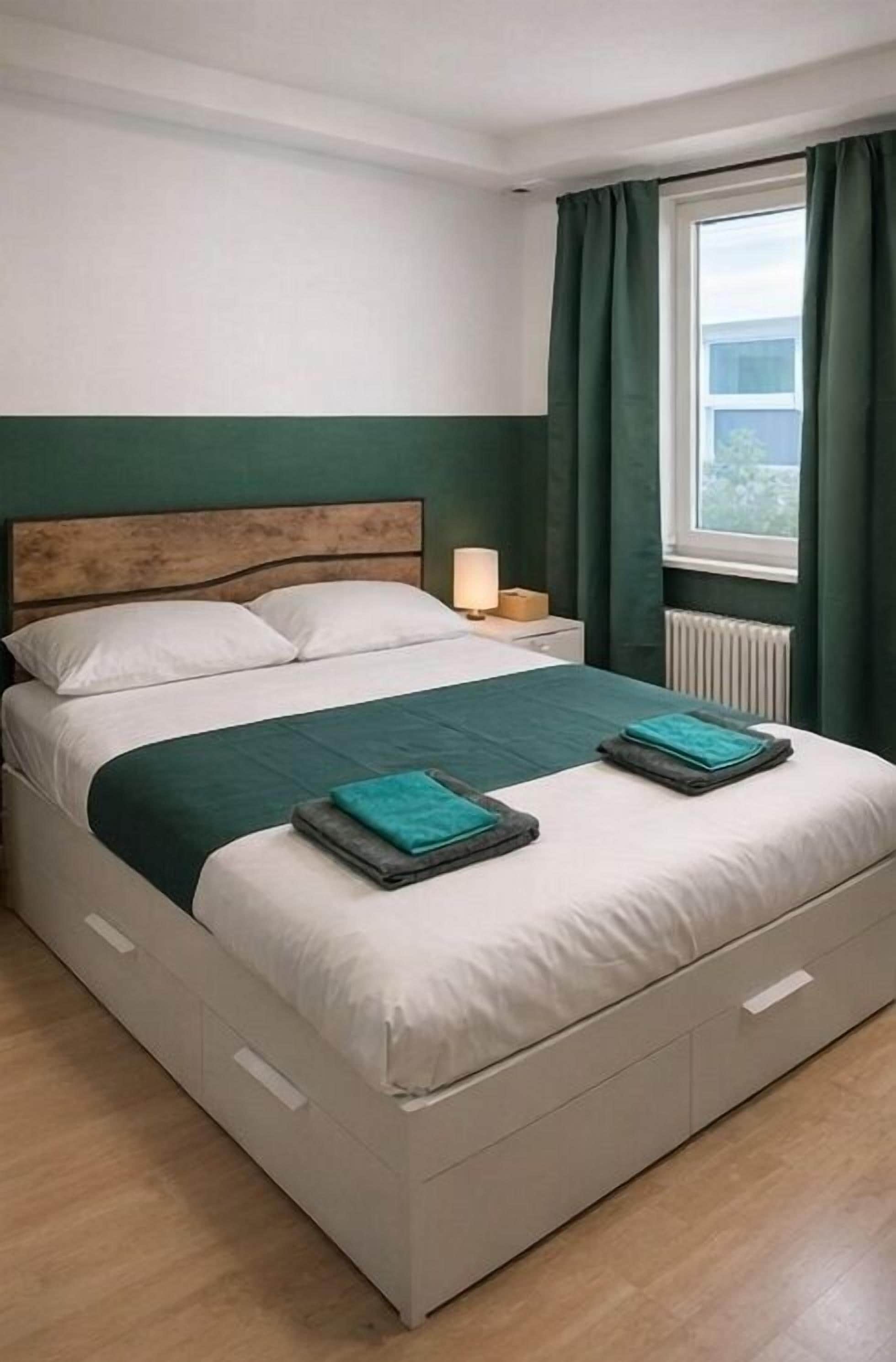 A bed with a wooden headboard, a bedside lamp, and a window with curtains.