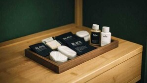 A wooden drawer with a BLACK brand toiletry set including a bar of soap, a toothbrush, and a bottle of hand sanitizer.