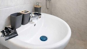 A bathroom with a white sink, a mirror, a shower, and two trash bins.