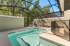 Ein Schwimmbad mit Glasveranda, umgeben von Sitzgelegenheiten im Freien und Blick auf Bäume.