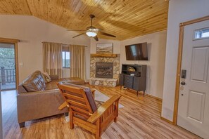 A living room with a stone fireplace, wooden furniture, a ceiling fan, and a TV mounted on the wall. - Camp Klip at Bison Ridge (Show Low)