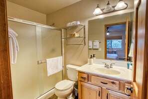 A bathroom with a glass shower enclosure, a toilet, a sink with a mirror, and wooden cabinets. - Camp Klip at Bison Ridge (Show Low)