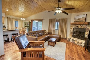 Ein gemütliches Wohnzimmer mit einem Ecksofa, Holzstühlen, einem Kamin und einem Deckenventilator.