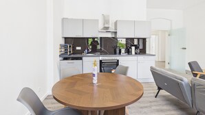 A modern kitchen with white cabinets, a round wooden dining table, and grey chairs. - Group apartment with balcony, up to 5 persons - GÖ05 (Görlitz)