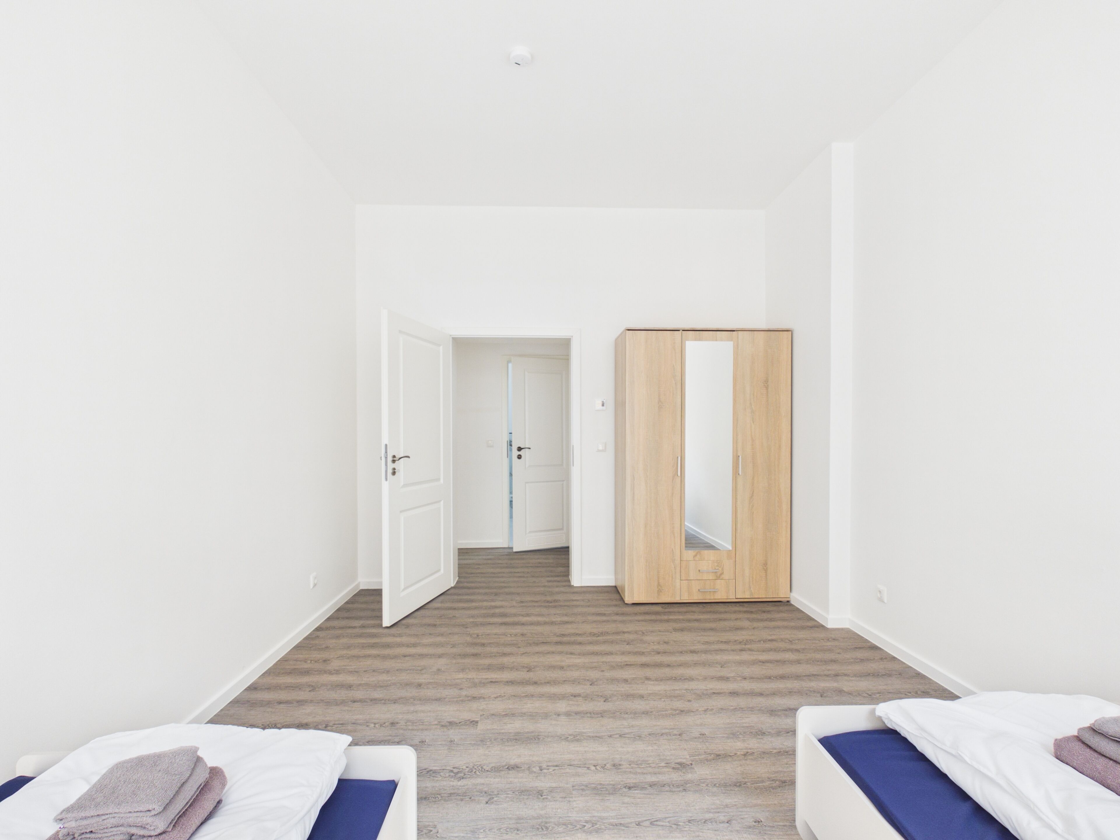 Habitación minimalista con dos camas, un armario y una puerta que da a otra habitación.