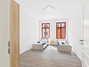A room with two beds, a wooden door, and a window with blinds. - Group apartment with balcony, up to 5 persons - GÖ05 (Görlitz)