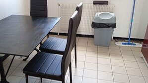 Huone, jossa on tummanvärinen pöytä ja tuolit, patteri, roskakori ja moppi.