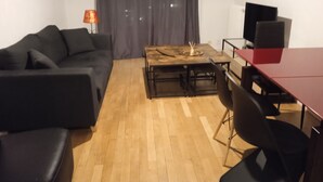 Moderni olohuone, jossa on sohva, sohvapöytä, televisio ja ruokapöytä.