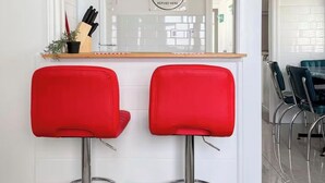A kitchen area with two red bar stools, a kitchen island, and a sign that reads 'Good Food Eat Served Here.' - Retro Retreat - Riverfront Access - St. Clair River (st clair)