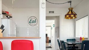 A modern kitchen with a 'Good Food Eat Served Here' sign, a dining area with a round table and chairs, and a bar area with red chairs. - Retro Retreat - Riverfront Access - St. Clair River (st clair)