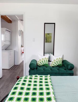 Un dormitorio con un sofá verde, una cama, un armario blanco y un espejo en la pared.