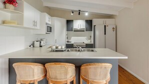 Una cocina moderna con armarios blancos, una isla central con lavamanos y tres taburetes de mimbre.