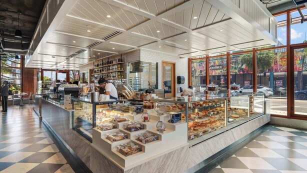 A bakery counter with various baked goods, a seating area with tables and chairs, and a view of the street outside. - Modern 2BR | Pool | Steps to Miami's Best Murals (Miami)