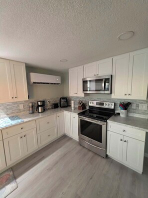 A modern kitchen with white cabinets, a stainless steel oven, a microwave, and a coffee maker. - Relax at Dark Island Gulf Retreat in this 4-bedroom house in Perry FL (Perry)