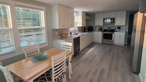 Een moderne keuken met witte kasten, een eettafel met stoelen en een koelkast.