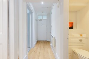 Een gang die leidt naar een badkamer met toilet, een radiator en een raam met uitzicht.
