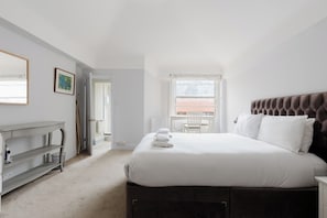 Een slaapkamer met een groot bed, een nachtkastje, een bureau en een raam met uitzicht.