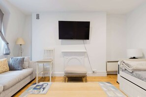 A modern living room with a sofa, a chair, a small table, a fireplace, a television mounted on the wall, and a bed with a blanket. - Brilliantly Located 1BD Flat by Piccadilly Circus (Greater London)