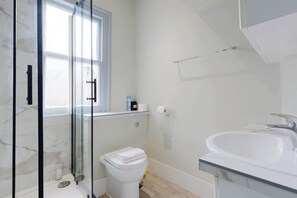A bathroom with a glass shower enclosure, a toilet, a sink, and a window. - Brilliantly Located 1BD Flat by Piccadilly Circus (Greater London)