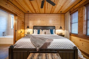 A wooden cabin bedroom with a bed, nightstands, a bench, a ceiling fan, and a window with blinds. - Private & Secluded - Hot Tub - Game Room - BBQ (Broken Bow)