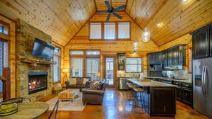 A spacious log cabin interior with a fireplace, a living area with a sofa and coffee table, a kitchen with modern appliances, and a dining area with a table and chairs. - Secluded Cabin, Hot Tub, Game Loft, 2 Fireplaces (Broken Bow)