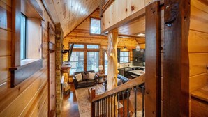 A wooden cabin interior with a loft bedroom, a dining area, and a kitchen. - Secluded Cabin, Hot Tub, Game Loft, 2 Fireplaces (Broken Bow)
