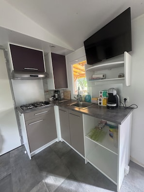 A compact kitchen with a gas stove, a sink, a microwave, and a flat-screen TV mounted above the counter. - Mobilhome 8 pers. Vineyard view near river peyroche Ruoms &Vallon-Pont-d'Arc (Labeaume)