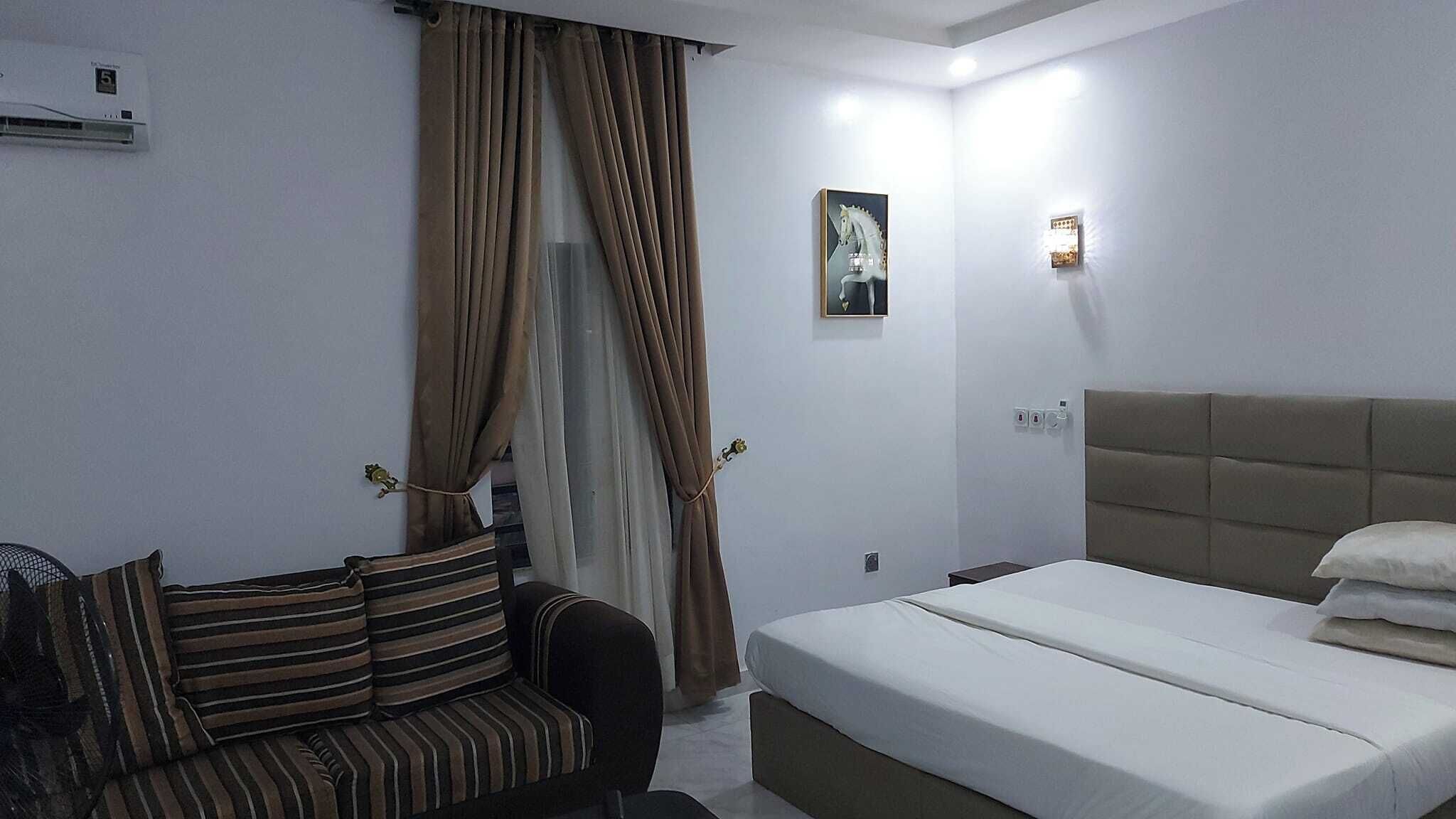 Ένα δωμάτιο ξενοδοχείου με ένα κρεβάτι, έναν καναπέ, ένα κλιματιστικό τοποθετημένο στον τοίχο, έναν πίνακα και ένα διακόπτη φωτός.