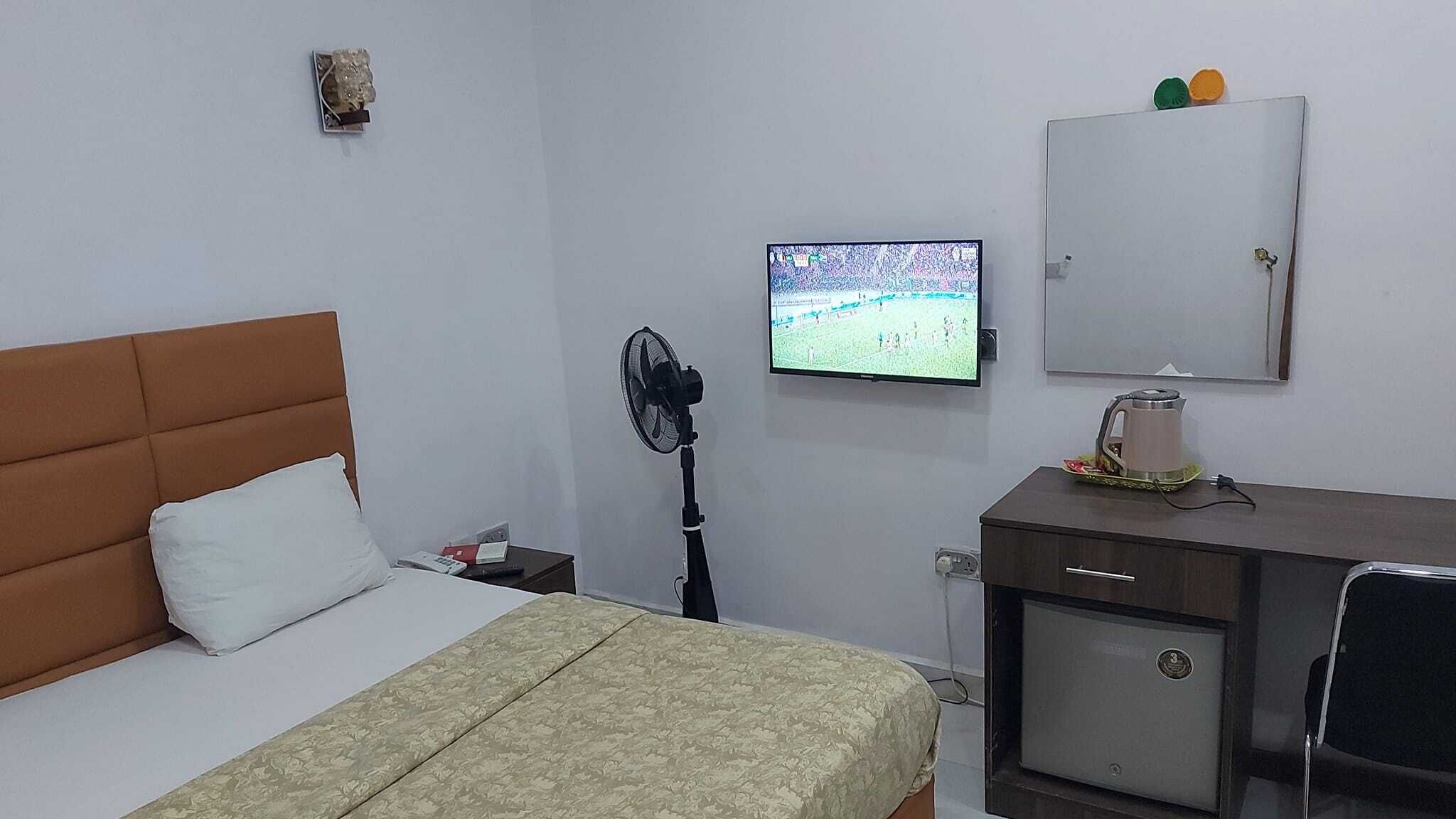 A hotel room with a bed, a desk, a chair, a TV, a fan, and a cabinet.