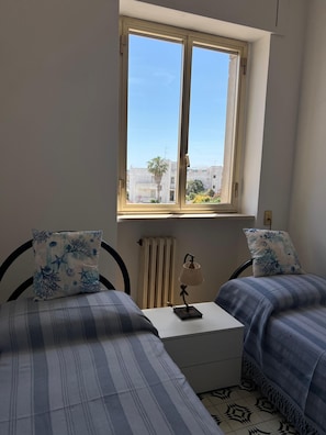 Ein Schlafzimmer mit zwei Betten, einem Fenster, einer Heizung und einer Lampe auf einem Nachttisch.