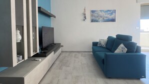 Una sala de estar moderna con un sofá azul, un televisor de pantalla plana y una pieza decorativa en la pared.