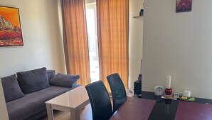 A room with a grey sofa, a white table, black chairs, a painting on the wall, and a window with curtains. - Two-room apartment 350 m from the beach, good infrastructure, quiet location (Sweti Wlas)